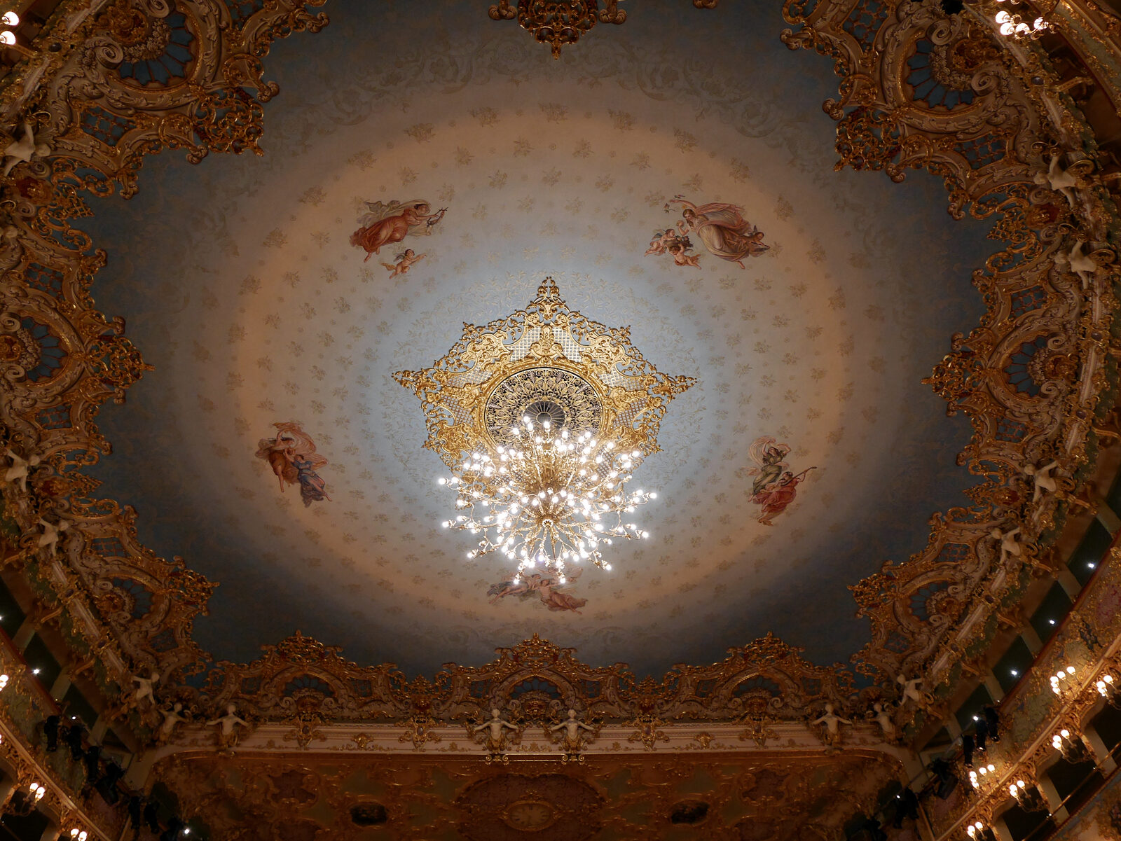 La Fenice : The ceiling features a large gilded chandelier at its center, surrounded by concentric circles in shades of blue that create the illusion of a dome, despite the ceiling being flat
