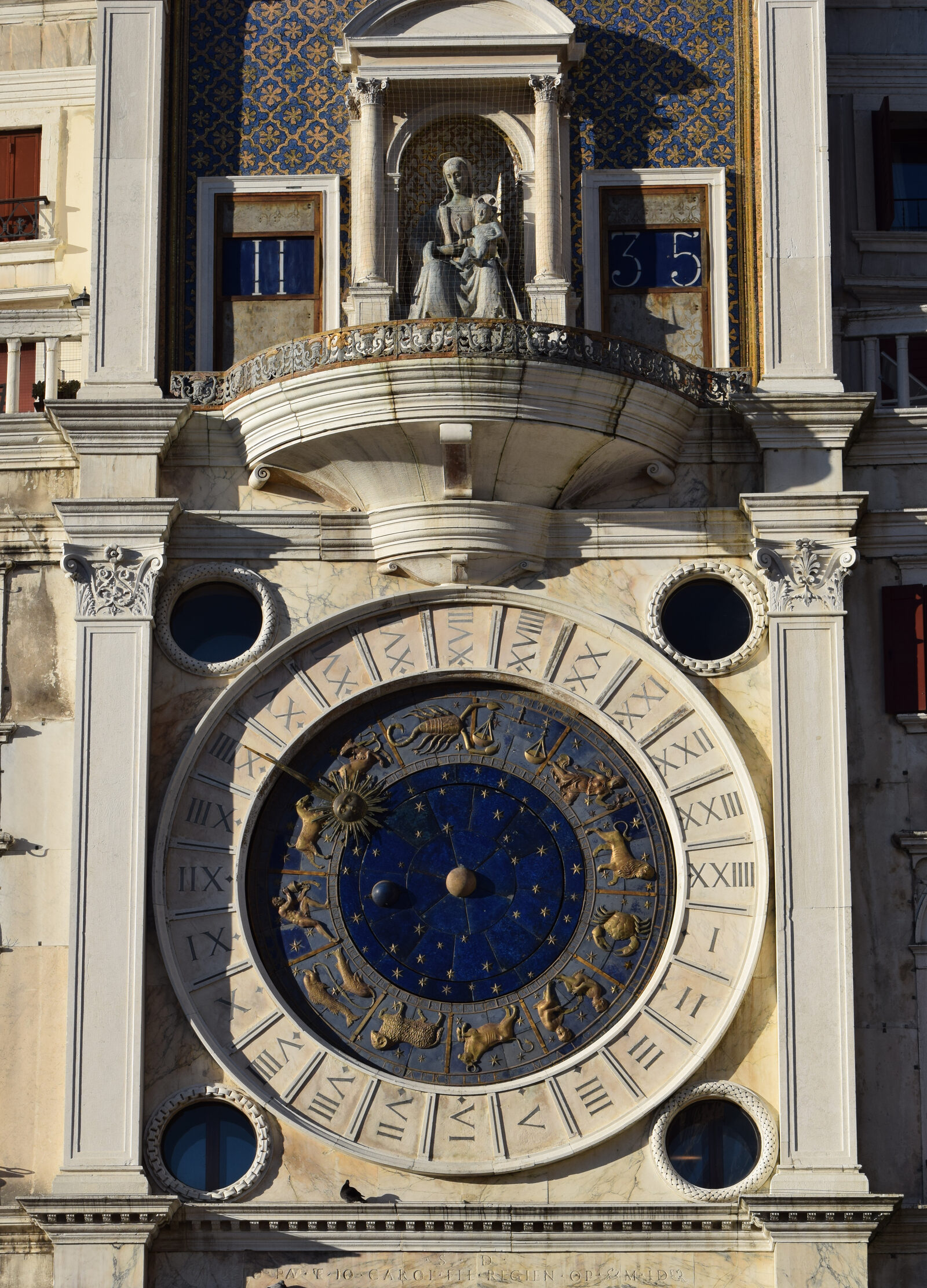 Clock Tower : The 24-hour dial with zodiac signs, above which sits the Virgin and child statue flanked by two barrels displaying hours and minutes